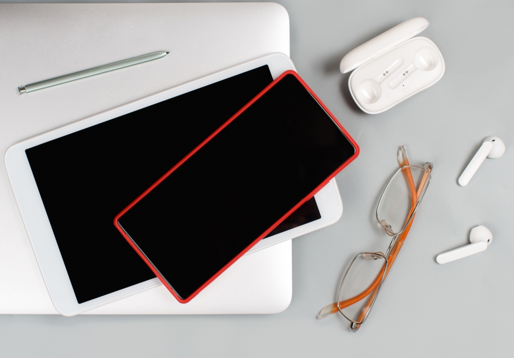 Mobile phone, tablet, earphones and glasses near laptop